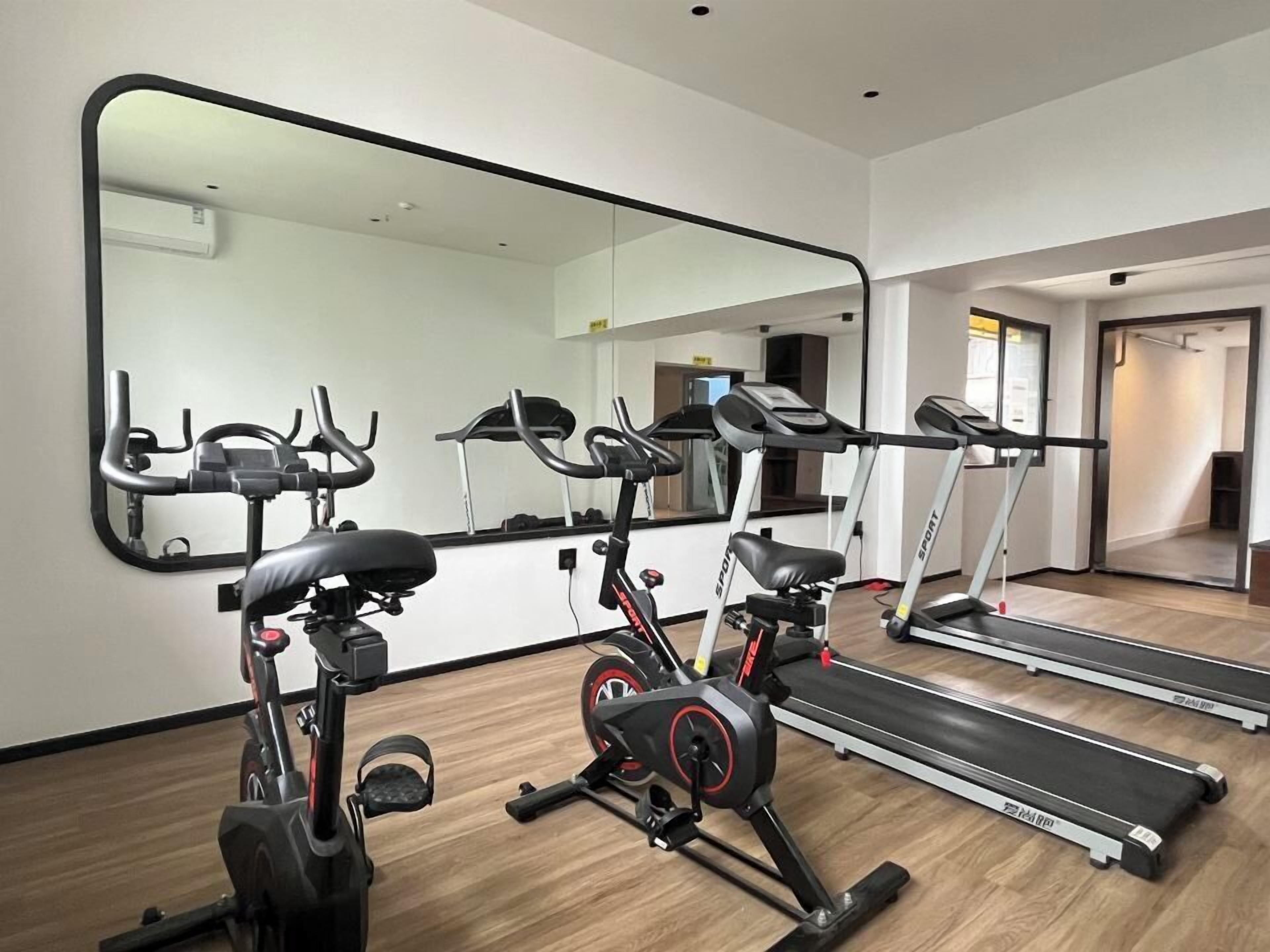 Et fitnessrum med motionscykler, løbebånd og et stort spejl.