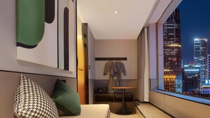 A modern hotel room with a large window offering a city view, a cozy seating area with a sofa and pillows, and a small table. - Mcsrh Hotel-Xi'an Xiaozhai  (Xi'an)