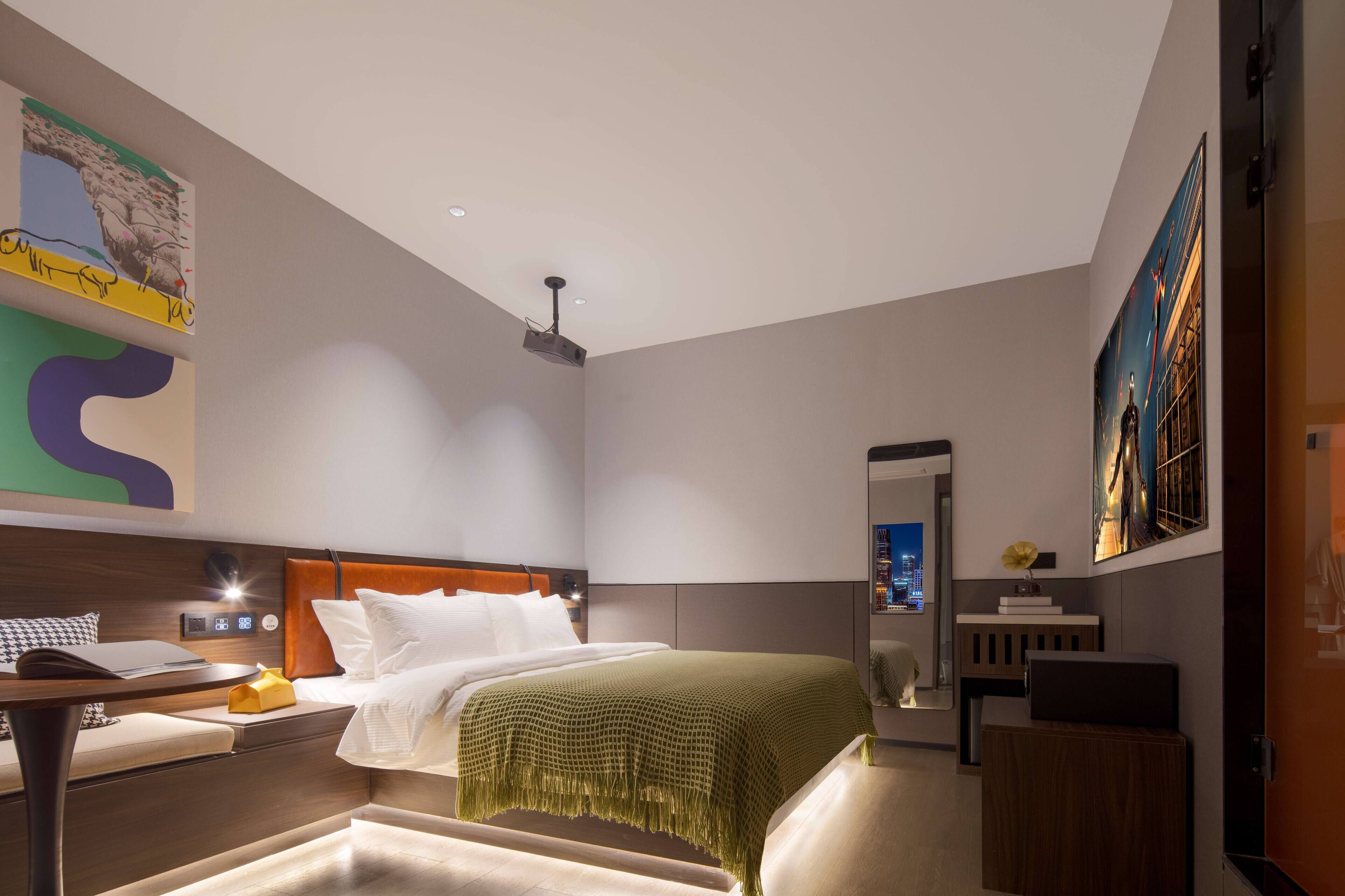 A modern hotel room with a bed, bedside table, lamp, and artwork on the walls.