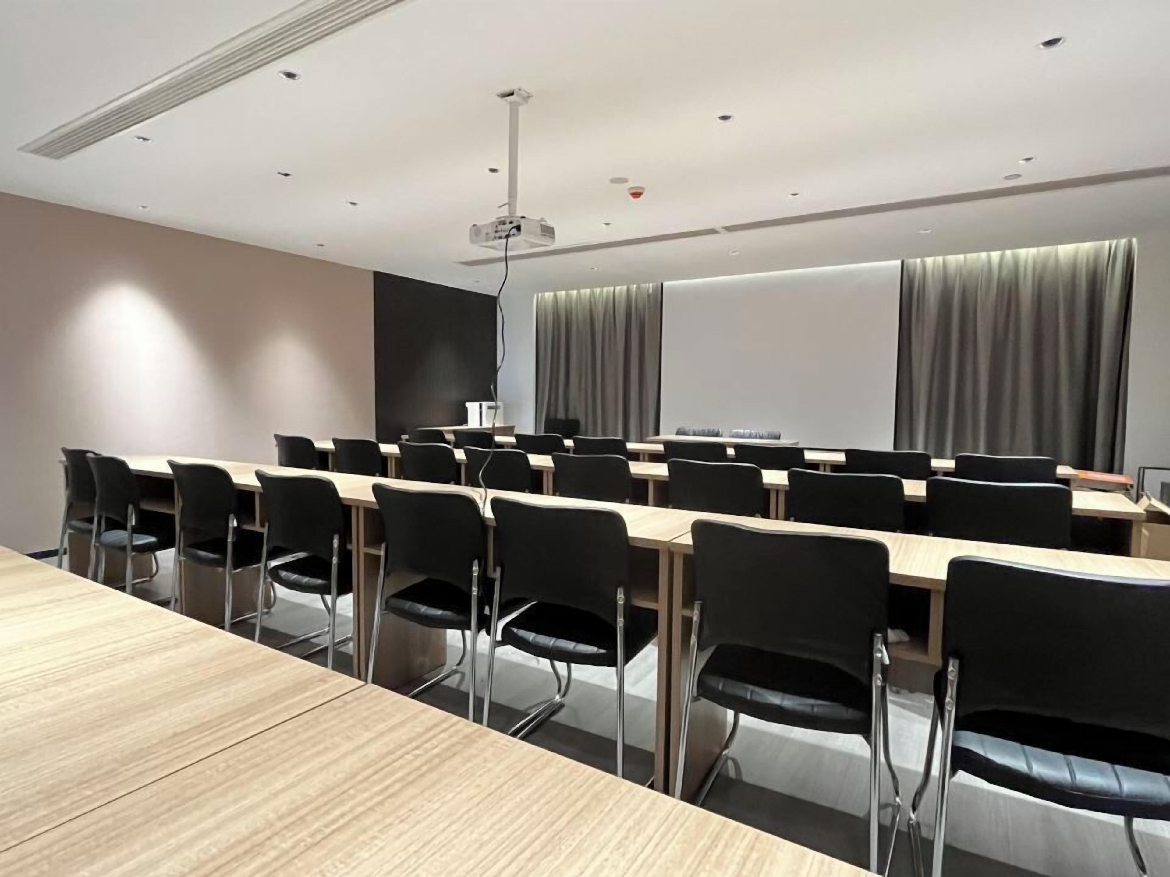 Un salón de conferencias con una larga mesa, sillas negras, un proyector y una pantalla.