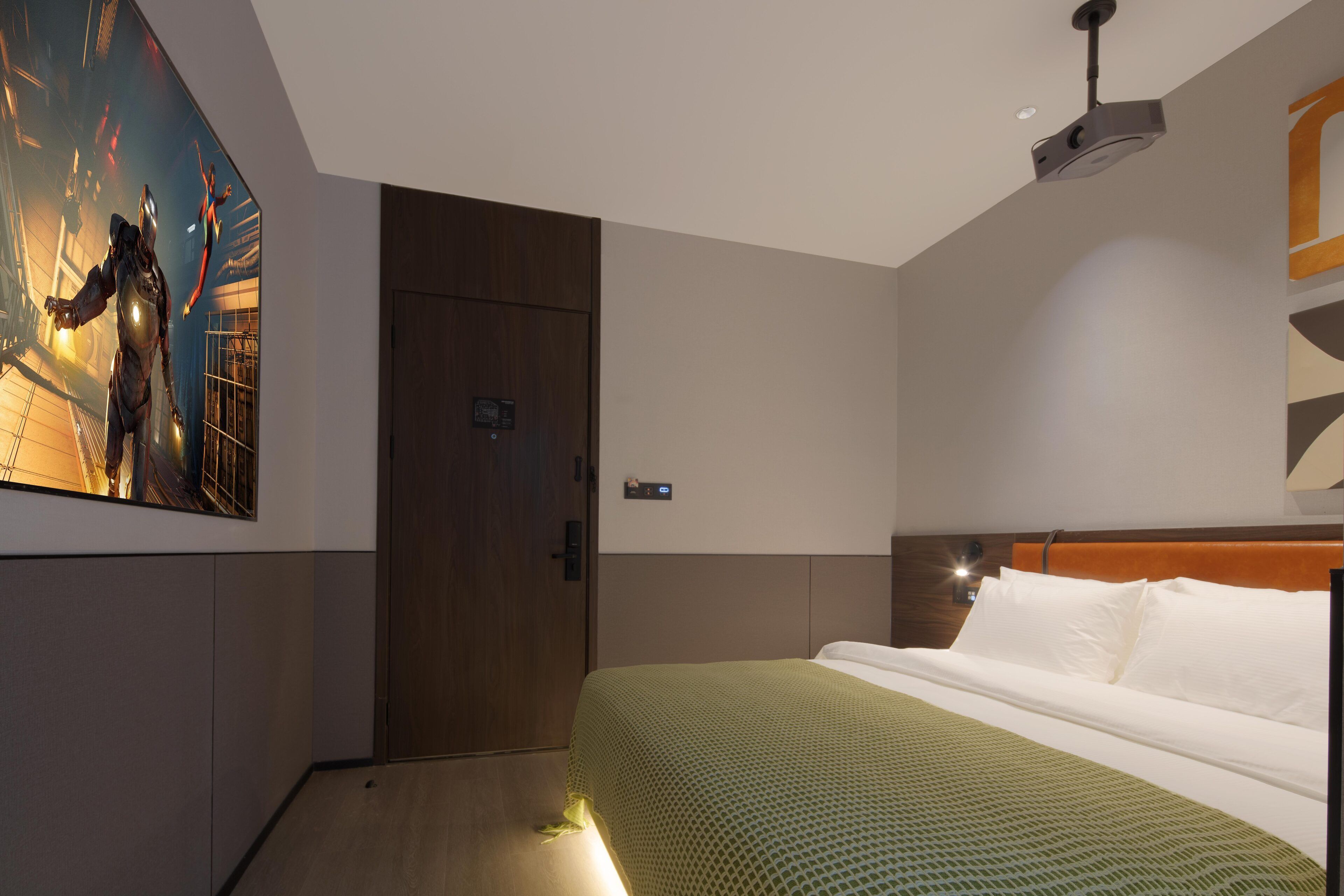 Habitación de hotel con cama, puerta de madera, proyector montado en la pared y un cartel en la pared.