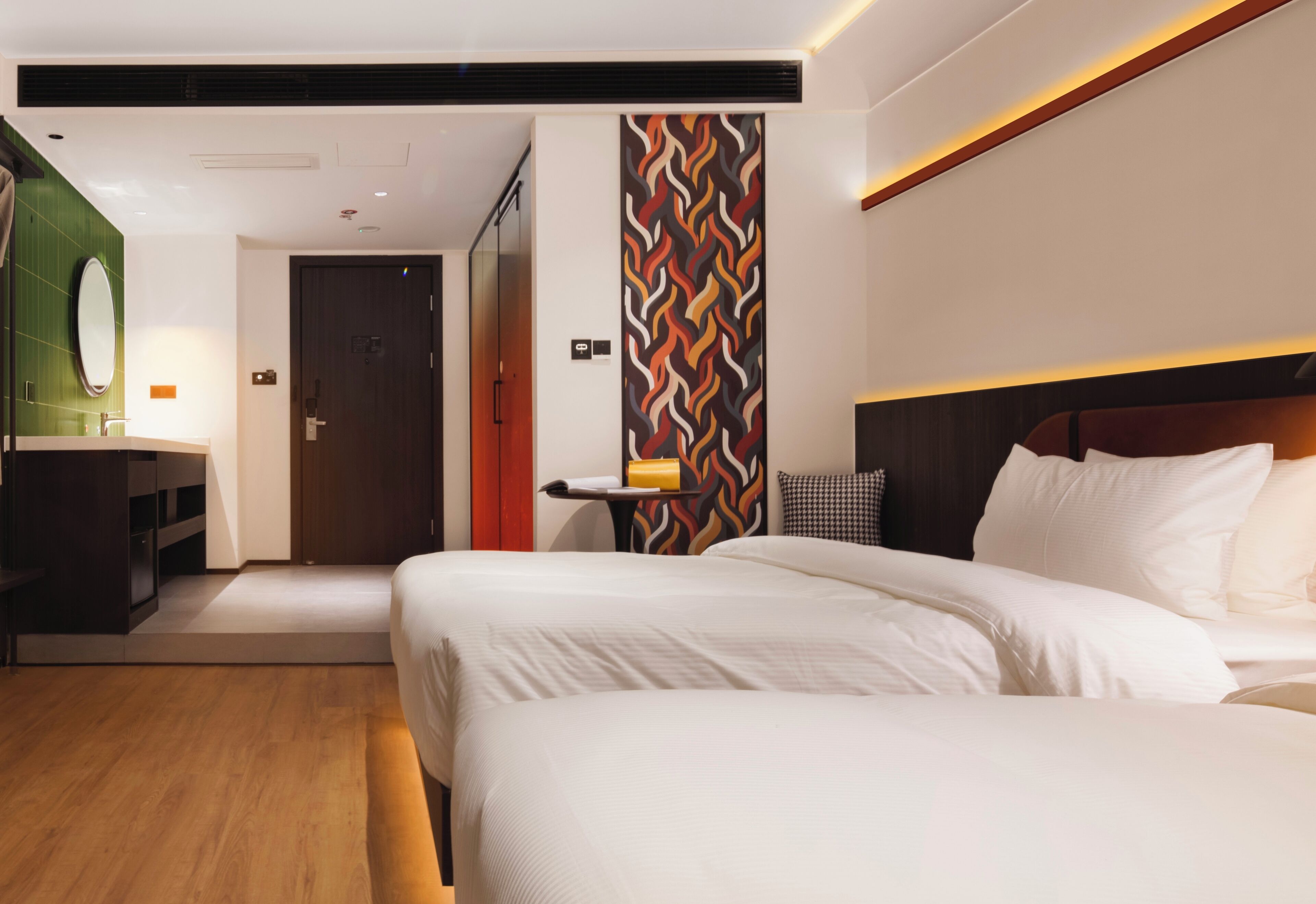 A hotel room with a large bed, a bedside table, a mirror, and a wall with a geometric pattern.