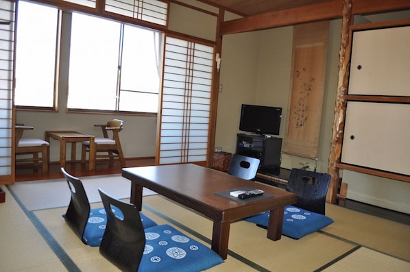 A traditional Japanese room with tatami mats, a low table, chairs, a television, and sliding doors. - Onomichi Yasuraginoyado Seeso (Onomichi)