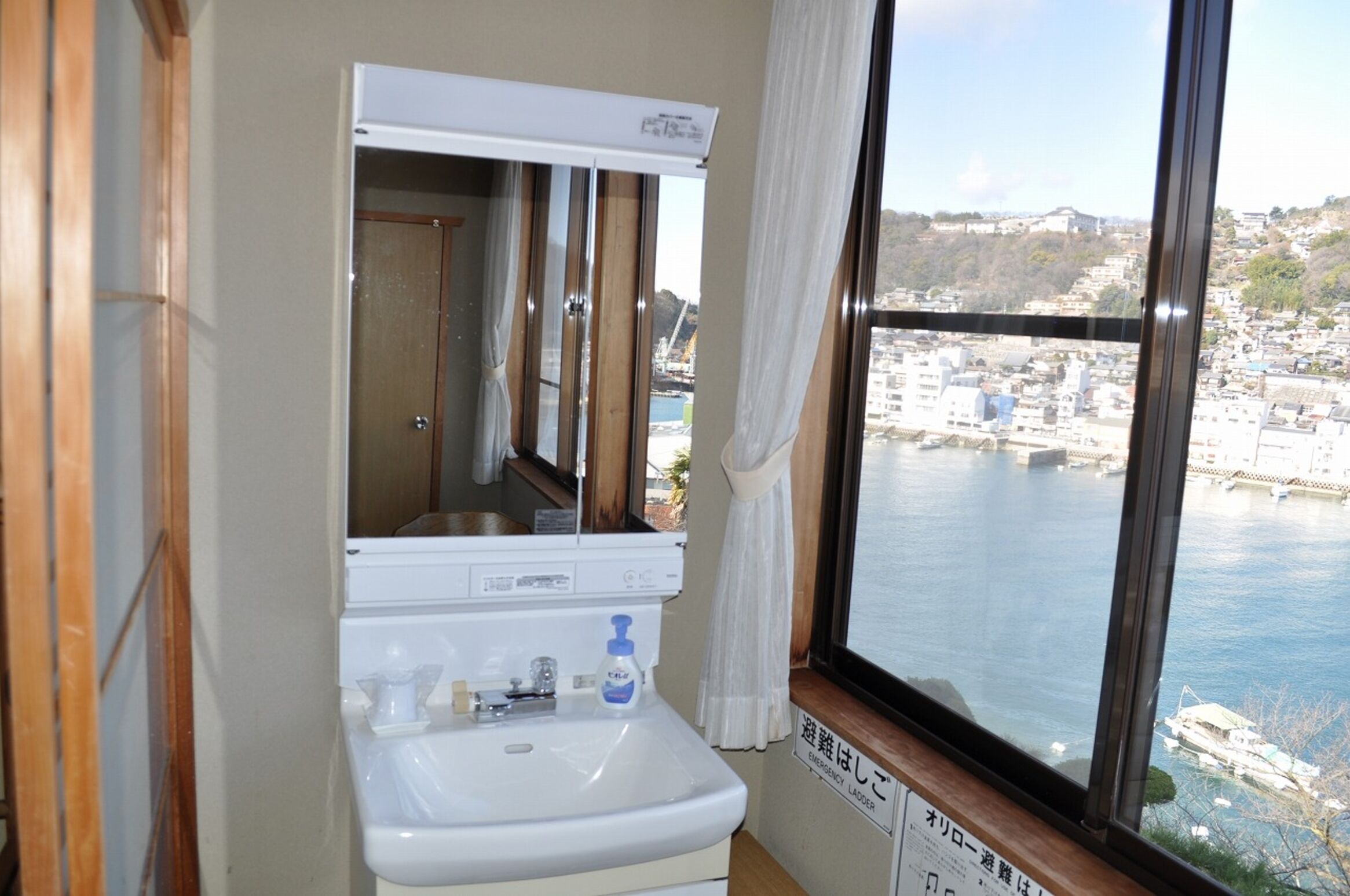 Une salle de bain avec un lavabo, un miroir et une fenêtre donnant sur un paysage urbain et l’eau.