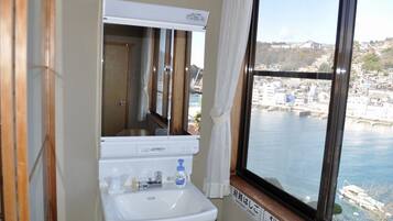 Une salle de bain avec un lavabo, un miroir et une fenêtre donnant sur un paysage urbain et l’eau.
