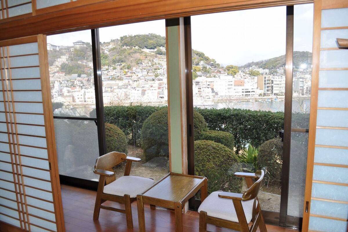 A room with a view of a cityscape through large windows, featuring a wooden table and chairs.