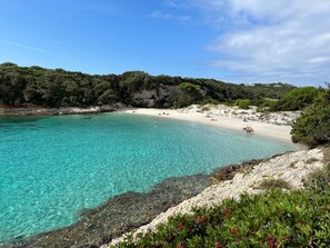 Enjoy a serene coastal escape with turquoise waters meeting a sandy beach, surrounded by lush greenery and rugged cliffs.