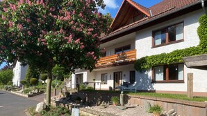 A two-story house with a balcony, a garden with various plants, and a sign indicating pet-friendly accommodation. - "Klein und Fein" Holiday Apartment – Your Getaway at Lake Edersee (Edertal)
