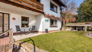 A two-story house with a balcony, a small patio with chairs, and a grassy yard. - "Klein und Fein" Holiday Apartment – Your Getaway at Lake Edersee (Edertal)