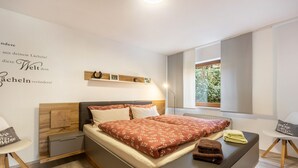 A modern bedroom with a bed, bedside tables, a window, and a wall with text and a clock. - "Klein und Fein" Holiday Apartment – Your Getaway at Lake Edersee (Edertal)