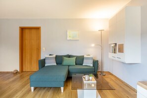 Een moderne woonkamer met een hoekbank, een vloerlamp en een kleine tafel met een plant.