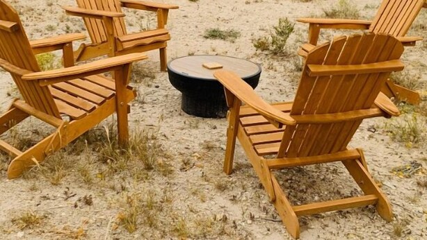 Fire træstole af Adirondack-design står i en cirkel rundt om et ildsted af sten i et ørkenlandskab.