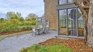 En moderne udendørs terrasse med en murstensvæg, en glasdør og et siddeområde med en sofa og stole.