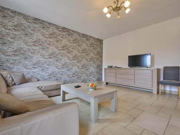 A living room with a stone wall, a sofa, a coffee table, a TV on a cabinet, and a chair.