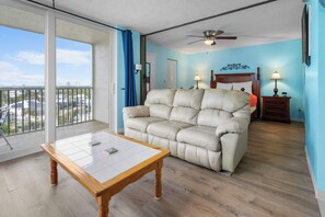 Ein Balkon mit Blick auf eine Stadtlandschaft, ein beiges Sofa, ein Holztisch und ein Deckenventilator.