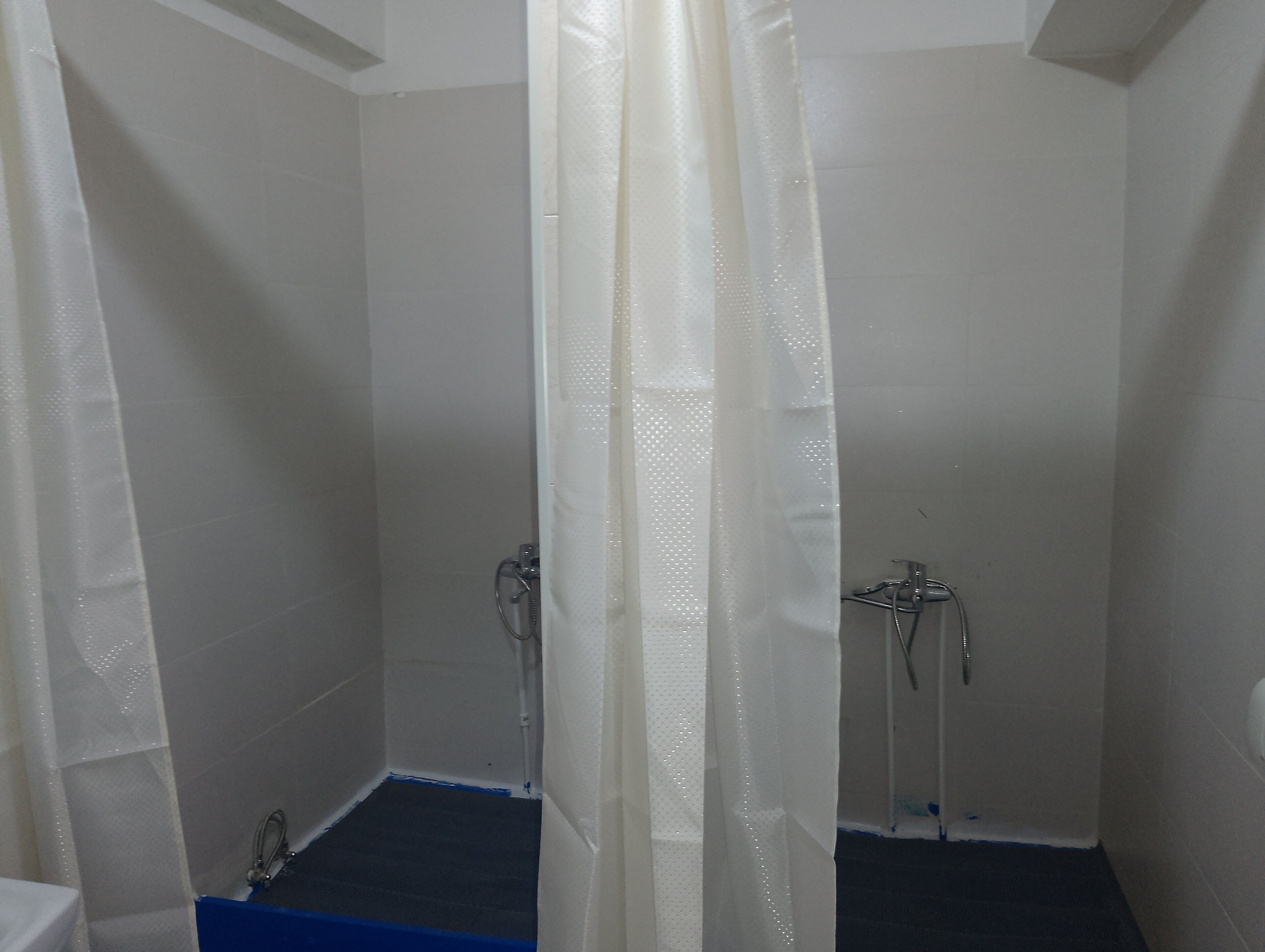 Un petit espace douche fermé, avec des murs blancs et un socle bleu.