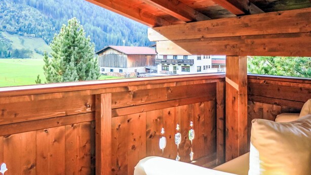 Ein hölzerner Balkon mit Blick auf eine Berglandschaft und ein Gebäude in der Ferne.