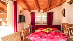 Ein Holztisch mit rotem Tischtuch, einer Obstschale und roten Vorhängen.