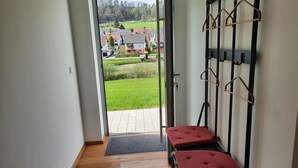 Een kamer met een houten vloer, een rode zacht beklede bank, een zwart bureau en een wandrek met haken.