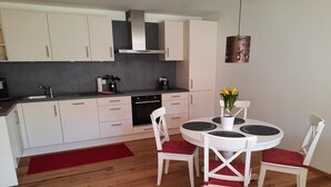 Een moderne keuken met witte kastjes, een zwart fornuis en een eethoek met een witte tafel en stoelen.