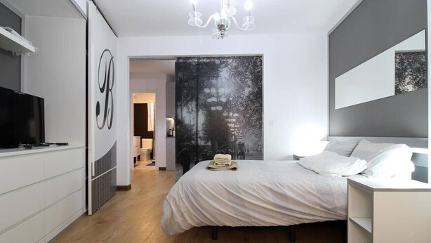 Ein modernes Schlafzimmer mit Bett, Fernseher, Kleiderschrank und großem Spiegel.
