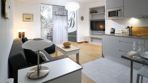 Ein modernes Wohnzimmer mit einer Couch, einem Couchtisch und einer Lampe. Es gibt eine Küchenzeile mit einer Mikrowelle und einem Spülbecken.