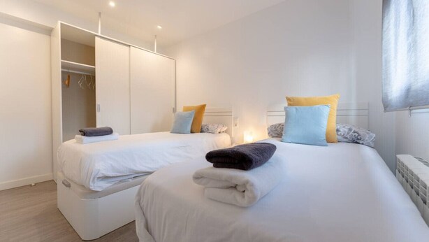 Ein modernes Hotelzimmer mit zwei Betten, einem begehbaren Kleiderschrank und einem großen Fenster.