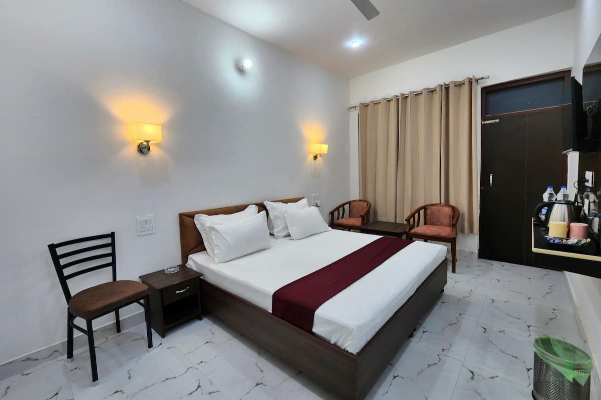 A hotel room with a bed, two chairs, a desk, a trash bin, and a wardrobe.