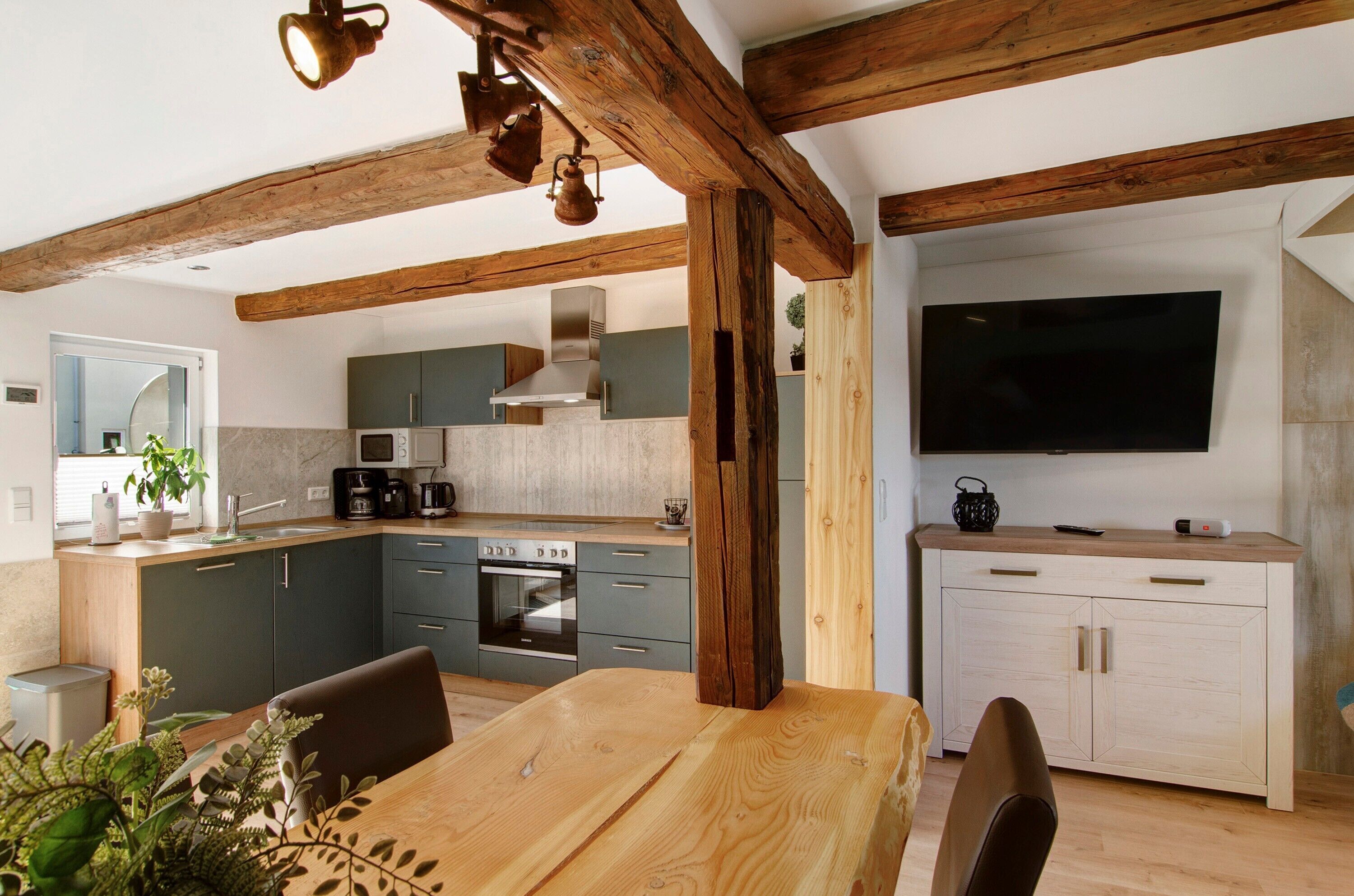 Una cocina moderna con vigas de madera, un comedor con mesa de madera y un televisor montado en la pared.