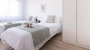 Habitación de hotel con dos camas, un armario, una ventana con cortinas translúcidas y un cuadro en la pared.