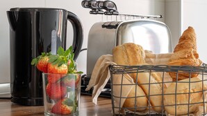 Una encimera de cocina con una cafetera negra, un tostador, una cesta de pan y un vaso de fresas.
