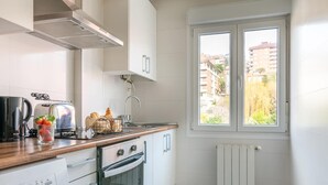 Cocina compacta con armarios blancos, horno empotrado, un lavamanos y una ventana con vistas a edificios.