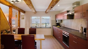 Een keuken met houten balken, een eettafel met stoelen en een raam met planten.