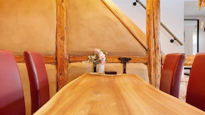 Een houten tafel met een bloevas, omringd door rode fauteuils in een kamer met zichtbare houten balken en een schuin dak.