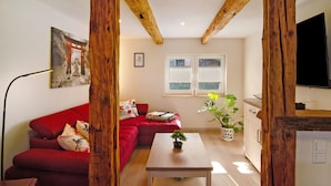 Een woonkamer met een rode bank, een houten tafel, een kamerplant en een televisie.