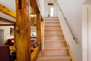 Un escalier en bois avec une rampe en bambou, un cadre de porte en bois et un canapé rouge à l’arrière-plan.