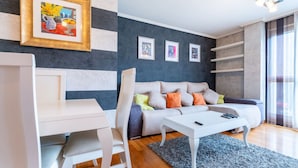 Ein modernes Wohnzimmer mit einer Couch, einem weißen Couchtisch und einem Schreibtisch. An der Wand hängen drei gerahmte Kunstwerke.
