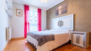 Ein Schlafzimmer mit Bett, Heizkörper, einem Fenster mit Vorhängen und einem an der Wand hängenden Kunstwerk.