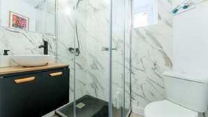 Ein Badezimmer mit einer gläsernen Duschkabine, einem weißen Waschbecken mit Holzablage und einem schwarzen Schrank mit Holzklinken.