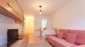 A living room with a TV, pink sofa, and a dining area with a table and chairs. - Fuentes de encanto en Santander 2 hab. (Santander)