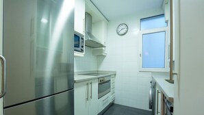 A compact kitchen with stainless steel appliances, white cabinetry, and a clock on the wall. - Fuentes de encanto en Santander 2 hab. (Santander)