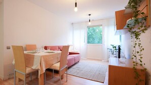 A dining area with a table set for four, a pink sofa, and a small kitchen area with a plant. - Fuentes de encanto en Santander 2 hab. (Santander)