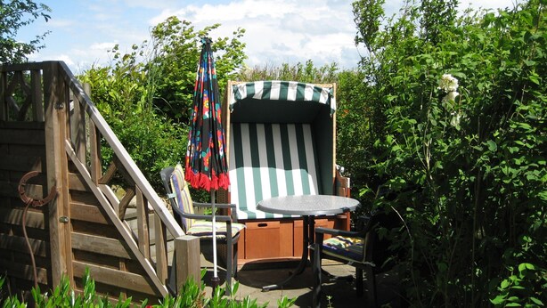 Una terraza de madera con una silla y una mesa, rodeada de follaje.