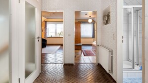 Un pasillo con suelo de baldosas, un radiador y una puerta de vidrio para la ducha.