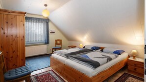 Un dormitorio con cama de madera, una silla, un armario, una ventana con cortinas y una lámpara.