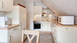Una cocina compacta con armarios blancos, microondas, cafetera y salpicadero de azulejos.