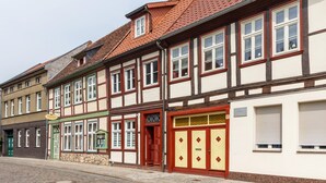 Une rangée de bâtiments traditionnels à colombages, dotés de nombreuses fenêtres et portes, dont certaines sont pourvues de volets, et une rue pavée.