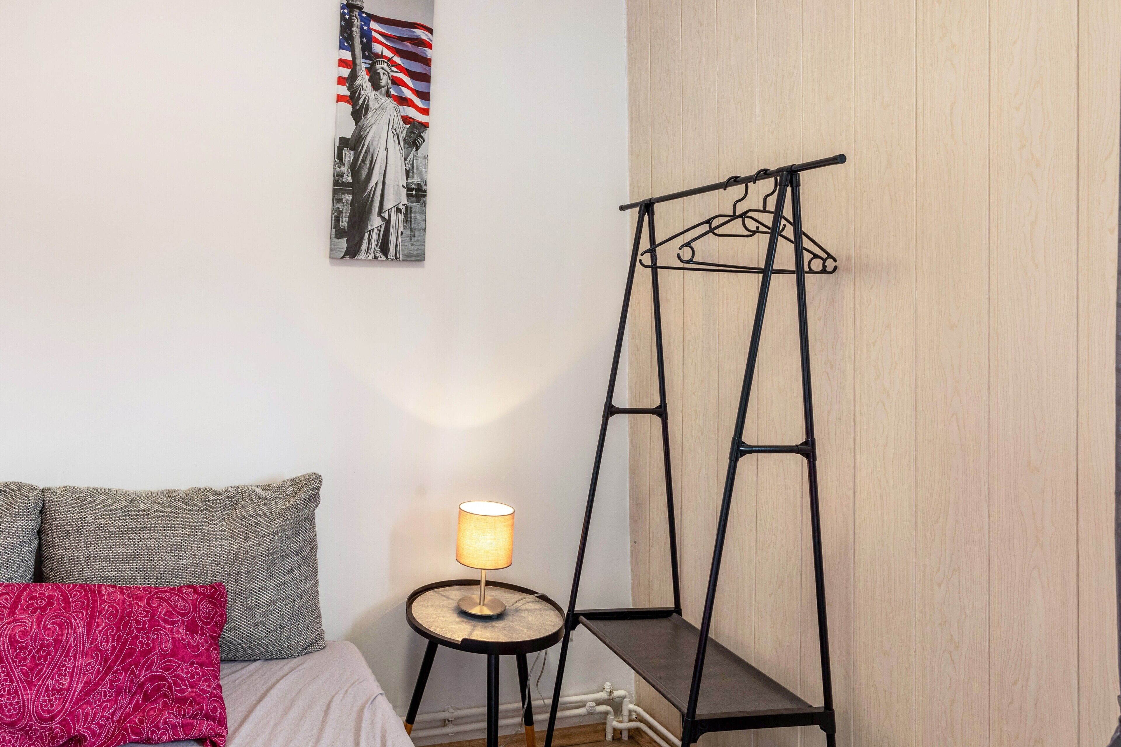 A bedroom with a bed, pillows, a lamp, a wall-mounted hanger, and a framed picture.