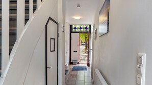 Un couloir avec un escalier, une porte, un radiateur et un interrupteur fixé au mur.