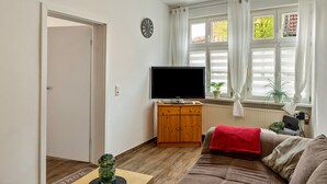 Un salon comprenant un téléviseur, un meuble en bois, un canapé et une fenêtre avec des rideaux.